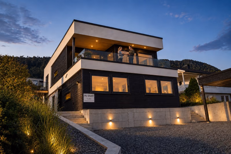 The Syvermarka house at dusk, with lit windows and an illuminated driveway
